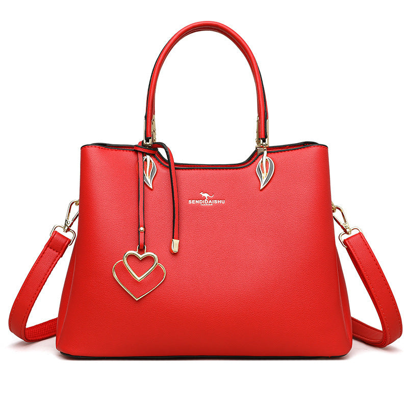 Women's shoulder bag in red with top handles, heart charm, leaf pulls, and crossbody strap