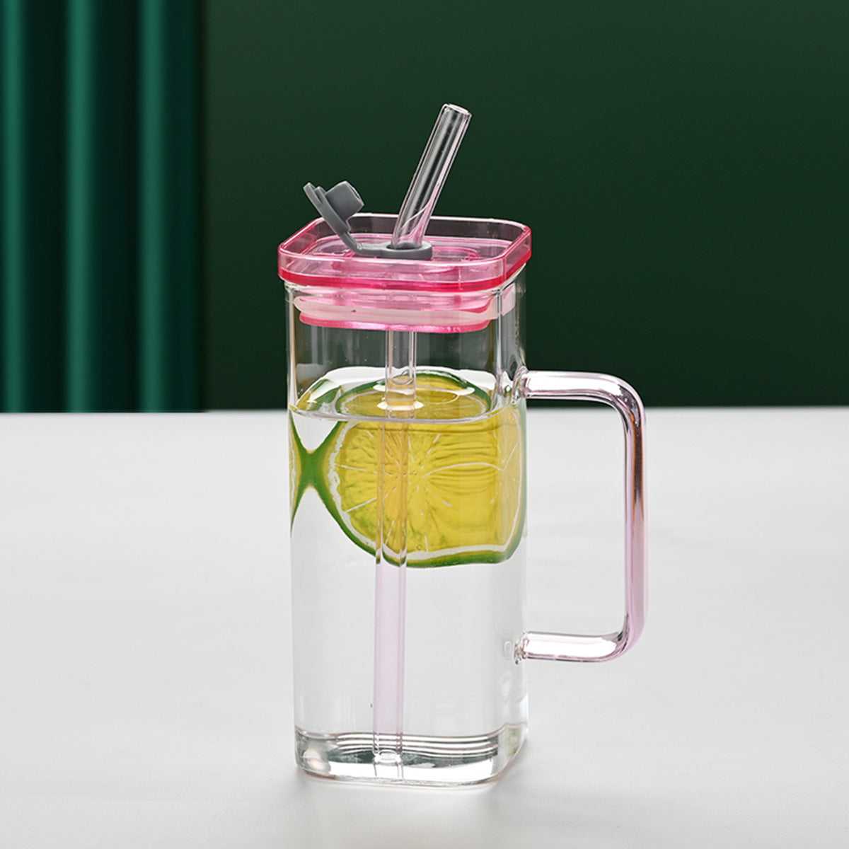 Clear square glass cup with pink lid, pink straw, and handle with lime slice