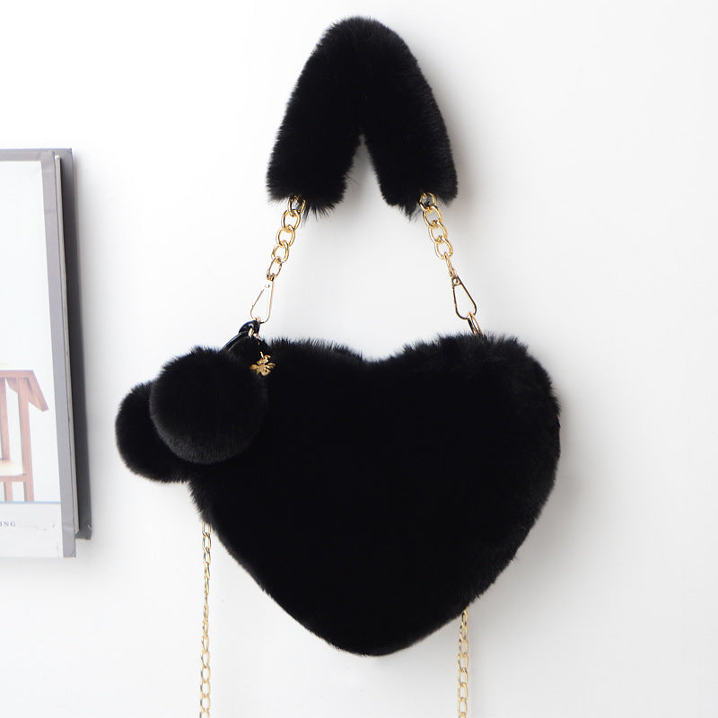 Black plush heart shoulder bag with gold chain and fuzzy pom-pom accents.