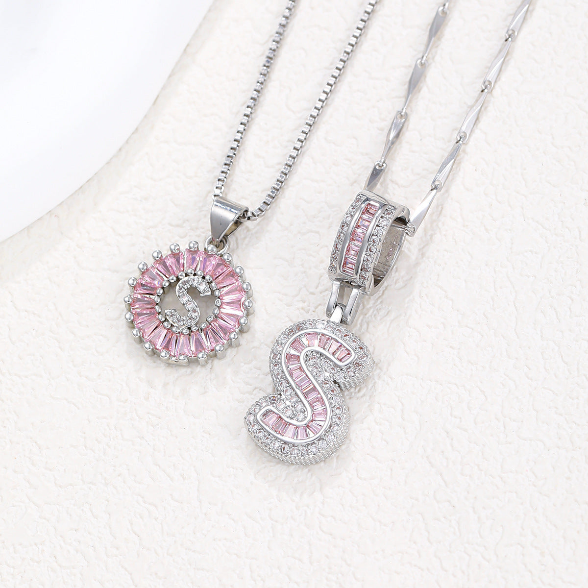Silver-tone pendant necklace set with pink zircon rosette pendant and rectangular block letter pendant.