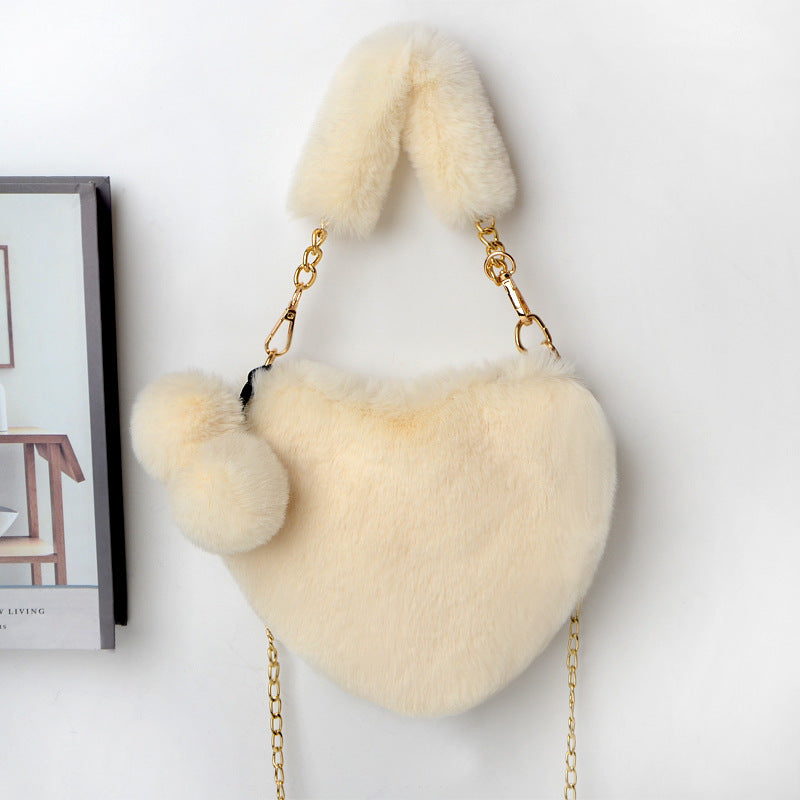 Heart-shaped plush handbag with pom-pom accents and gold chain strap, off-white