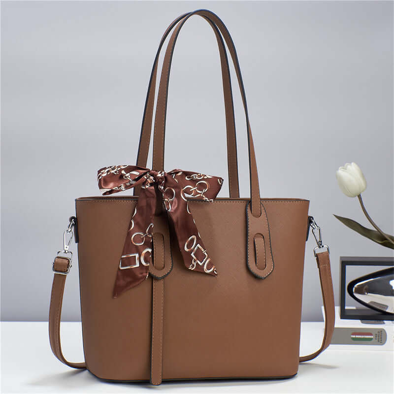 Brown tote handbag with top handles, front zipper pocket, and decorative metal charm details.