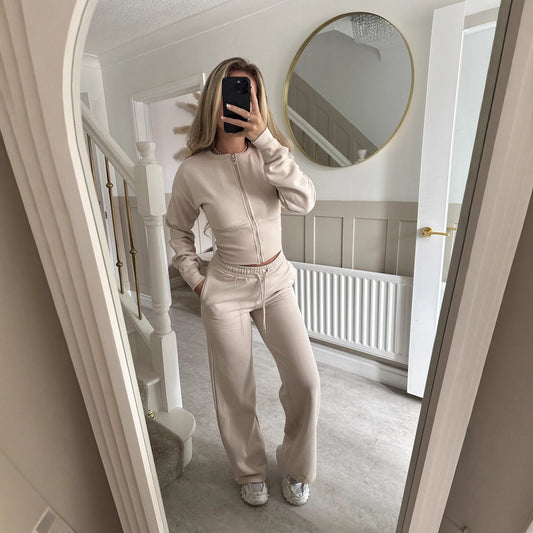 A woman modeling a high-fashion casual suit set in a neutral tone, featuring a tailored blazer-style jacket and coordinating trousers for a modern Western aesthetic.