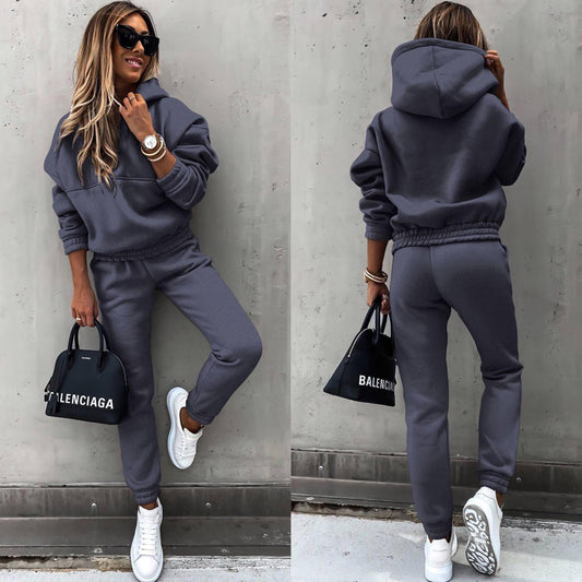 A woman modeling a matching solid-color tracksuit set featuring a drawstring hooded sweatshirt and tapered slim-fit joggers with elastic cuffs.