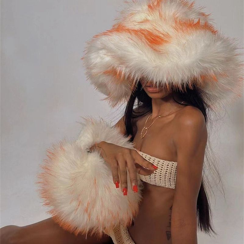 A person holding a plush bag with artificial raccoon fur in white and orange colors, featuring a round shape and tassels.