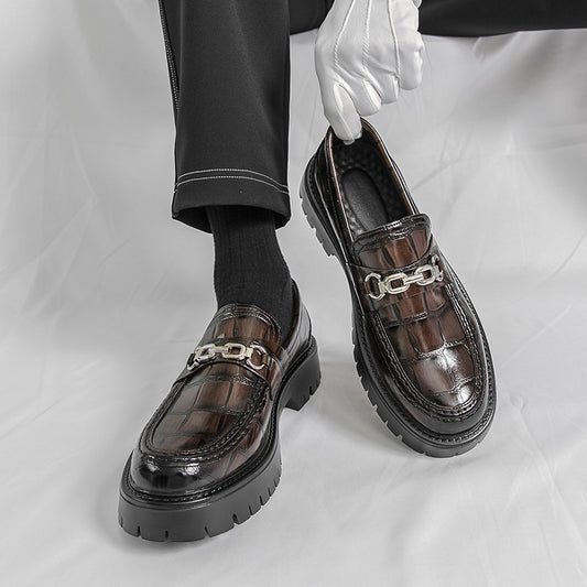Brown leather shoes with chain details worn by a person on a white background