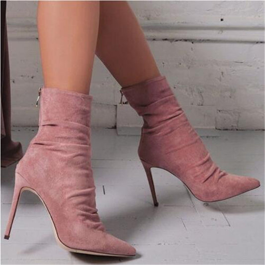 A pair of pink wrinkled suede high heel boots with a pointed toe and stiletto heel.