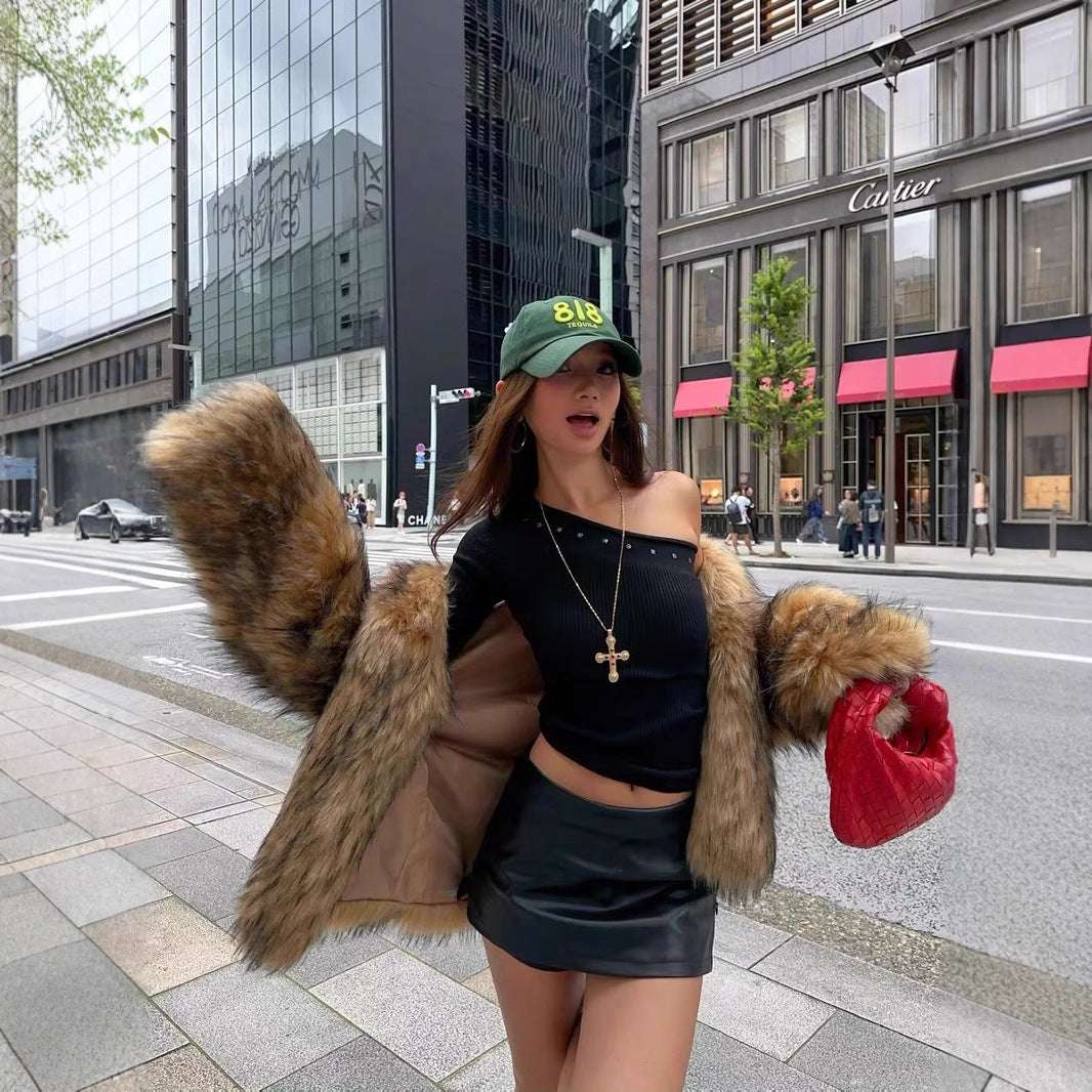 Person wearing a black outfit with fur accents and a green cap on a city street.