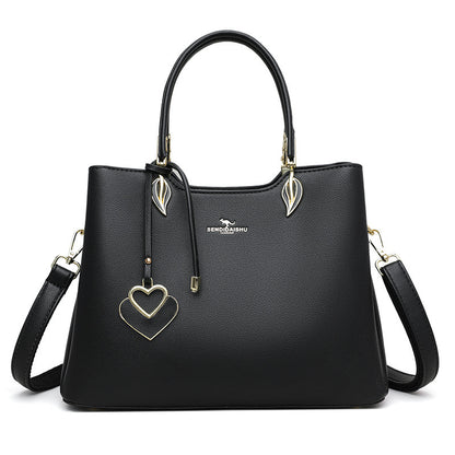 Black women’s shoulder bag with top handles, heart charm, and gold-tone crossbody strap