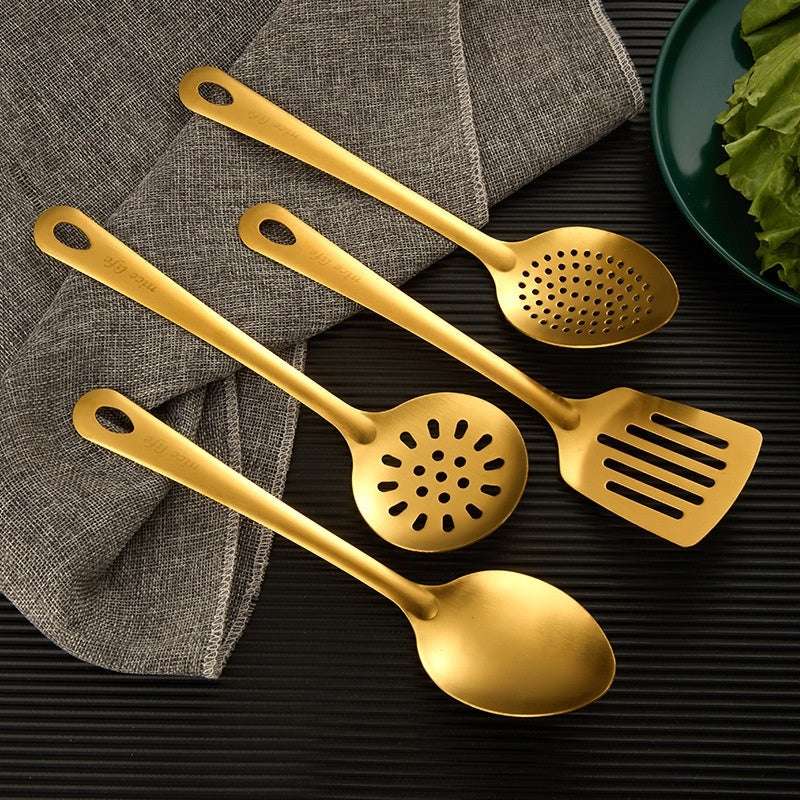 Set of gold kitchen utensils including a spoon, spatula, and skimmer on a dark surface.