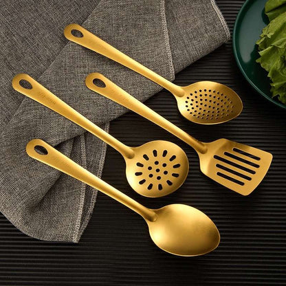Set of gold kitchen utensils including a spoon, spatula, and skimmer on a dark surface.