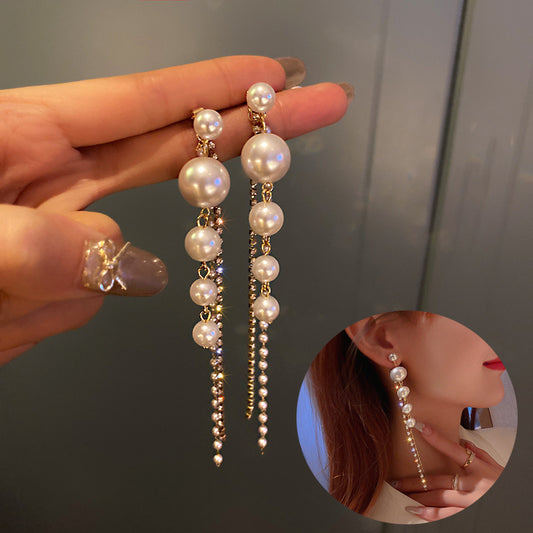Pearl earrings held by a hand with a close-up of an ear wearing them.