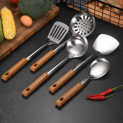Set of kitchen utensils with wooden handles on a dark surface with vegetables in the background.