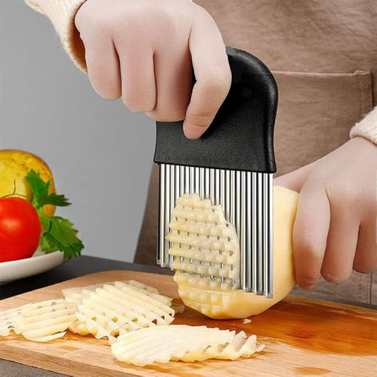 Stainless steel crinkle cutter blade slicing through a potato to create wavy french fry shapes on a kitchen cutting board