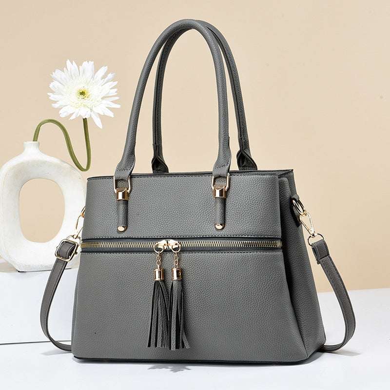 A large capacity soft leather shoulder bag with a tassel design, displayed in a horizontal square shape. The bag has a combination of colors including black and red, with a visible zipper and a tassel hanging from the main compartment.