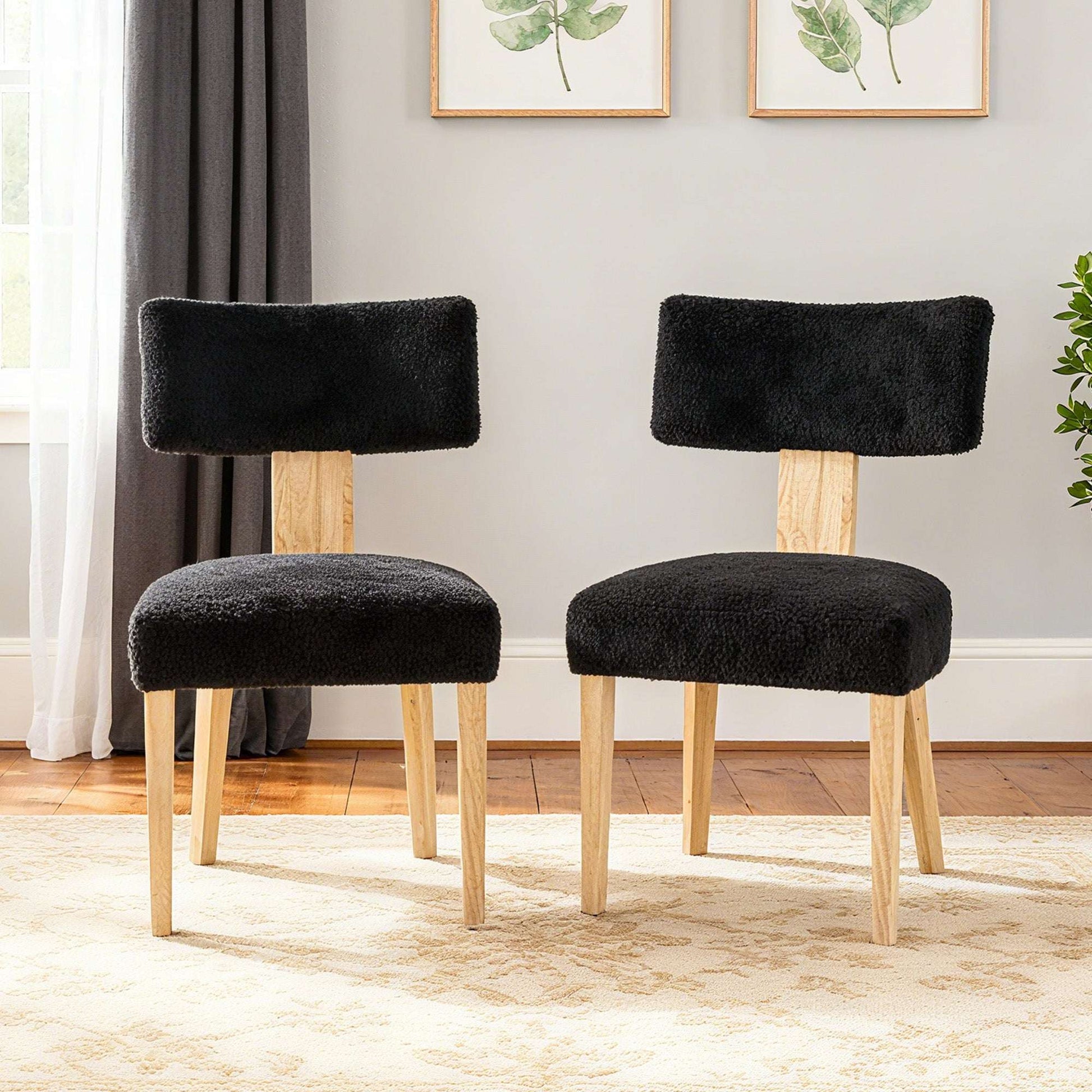 Pair of black upholstered dining chairs with light wood legs and padded backrests