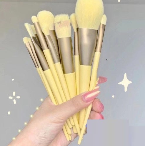 Makeup brush set with yellow handles and light beige bristles, held as a fan