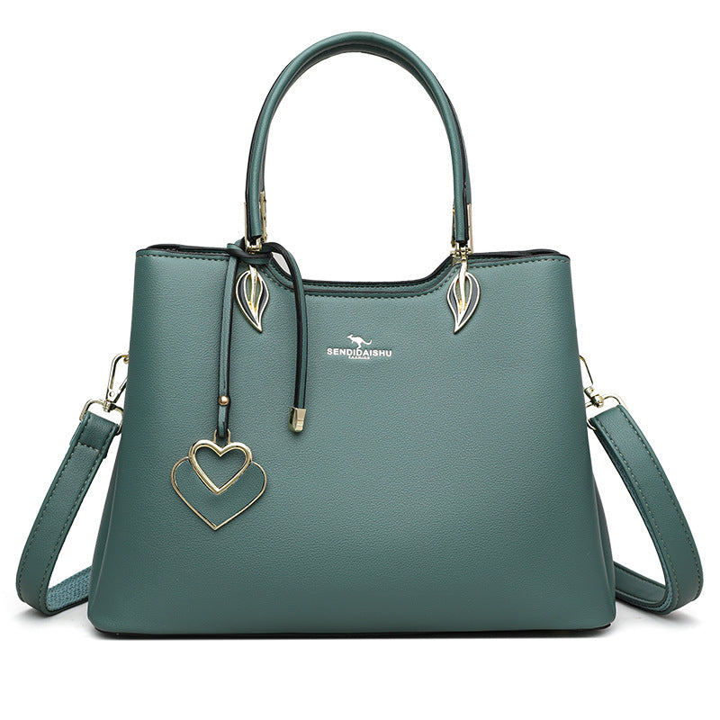 Green women’s shoulder bag with top handles, heart charm, and adjustable crossbody strap