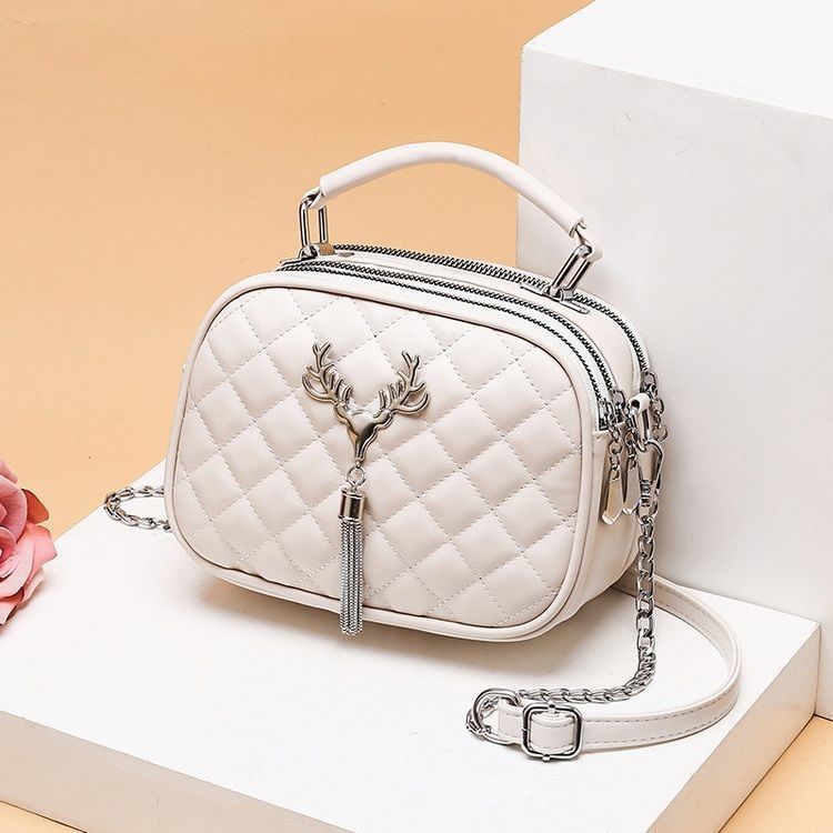 White quilted oval handbag with top handle, chain strap, deer emblem and tassel zipper pull