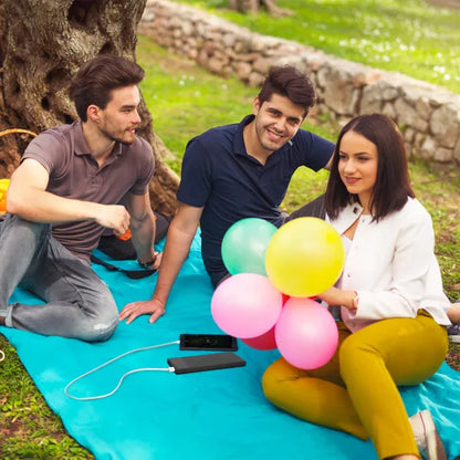 Black ultra-thin power bank connected outdoors on a picnic blanket near balloons.