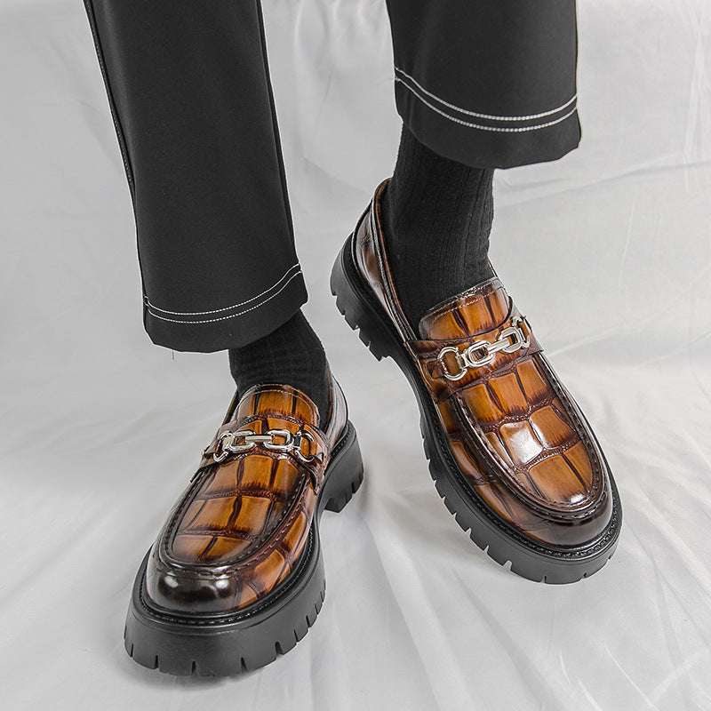 Brown leather shoes with chain details worn by a person on a light gray background