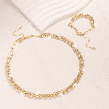Rhinestone leaf jewelry set in gold tone: necklace and bracelet laid out on fabric.