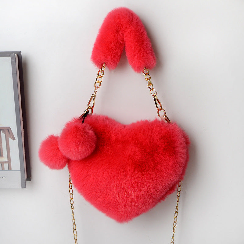 Heart-shaped plush handbag with pom-pom accents and gold chain strap, bright red