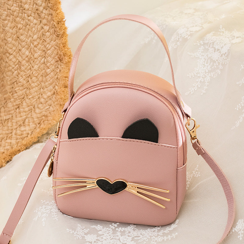 Pink mini cat-face crossbody backpack with black ears, gold heart whisker bar, and strap