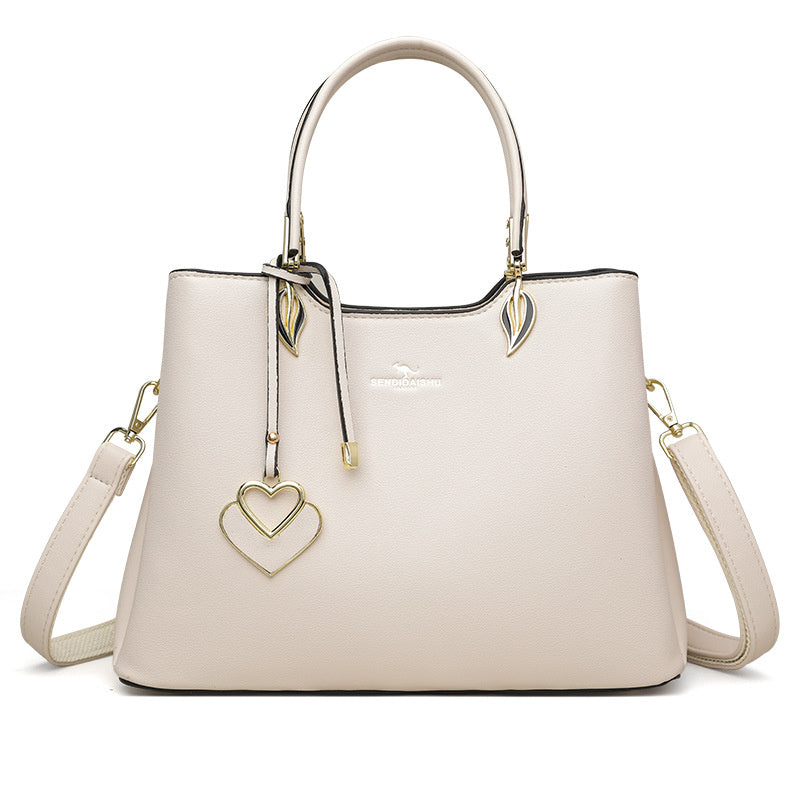 Light beige women’s shoulder bag with top handles and side crossbody straps with charms