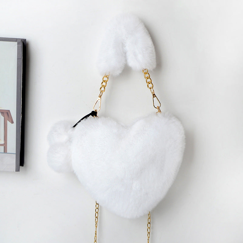 Heart-shaped plush handbag with pom-pom accents and gold chain strap, white