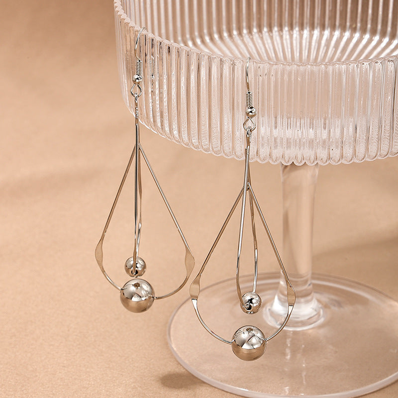 Silver hollow water drop tassel earrings with round charm drops, on clear stand