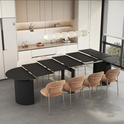 Black extendable dining table with long multi-panel top and ribbed pedestal base near chairs.