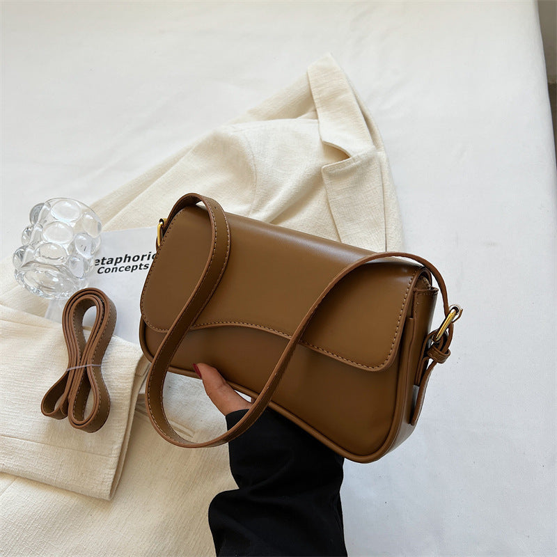 Brown shoulder bag with flap and magnetic buckle, curved panel seams, crossbody strap