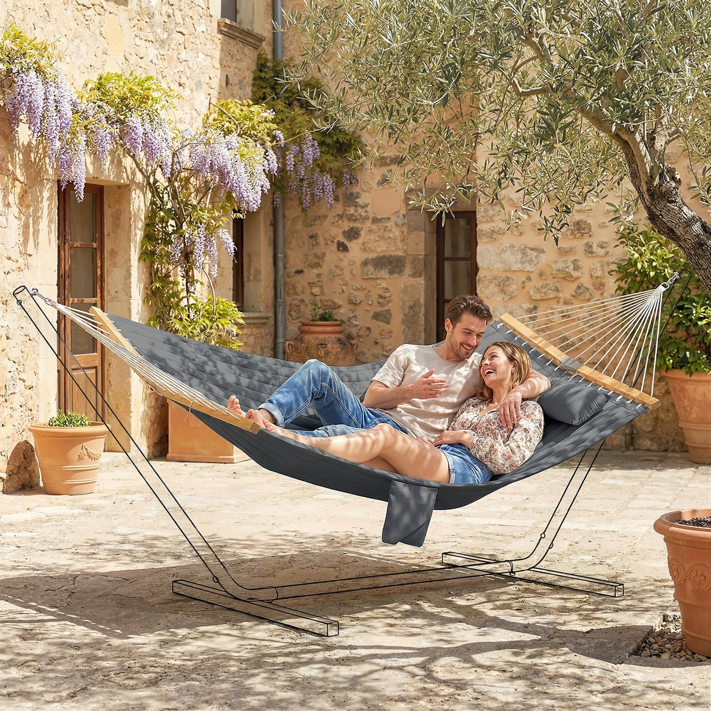 Gray two-person outdoor hammock with pillow, two adults reclining on the padded bed
