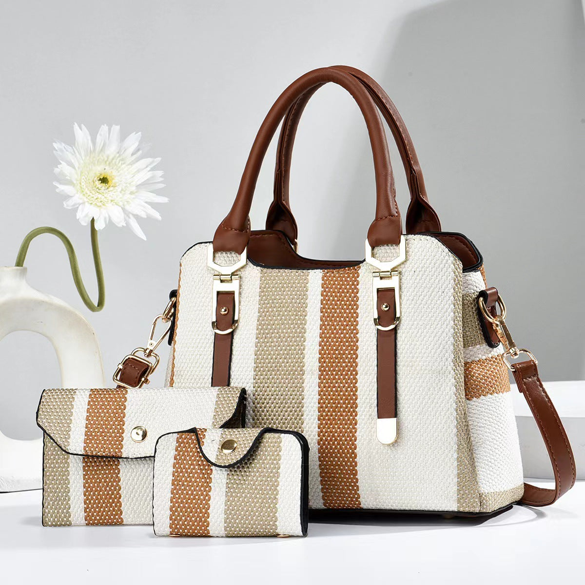 Striped handbag with brown accents on a white surface with a flower in the background