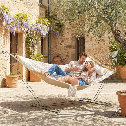 Two-person cream hammock with pillow and wooden spreader bars, two people at rest