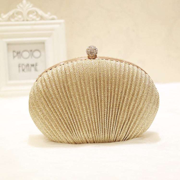Gold glitter oval shell clutch with jeweled clasp, front view on solid background