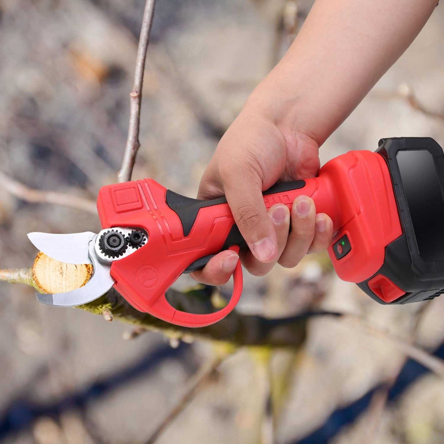 Red cordless pruning shears held by hand, with white blade and cutting head