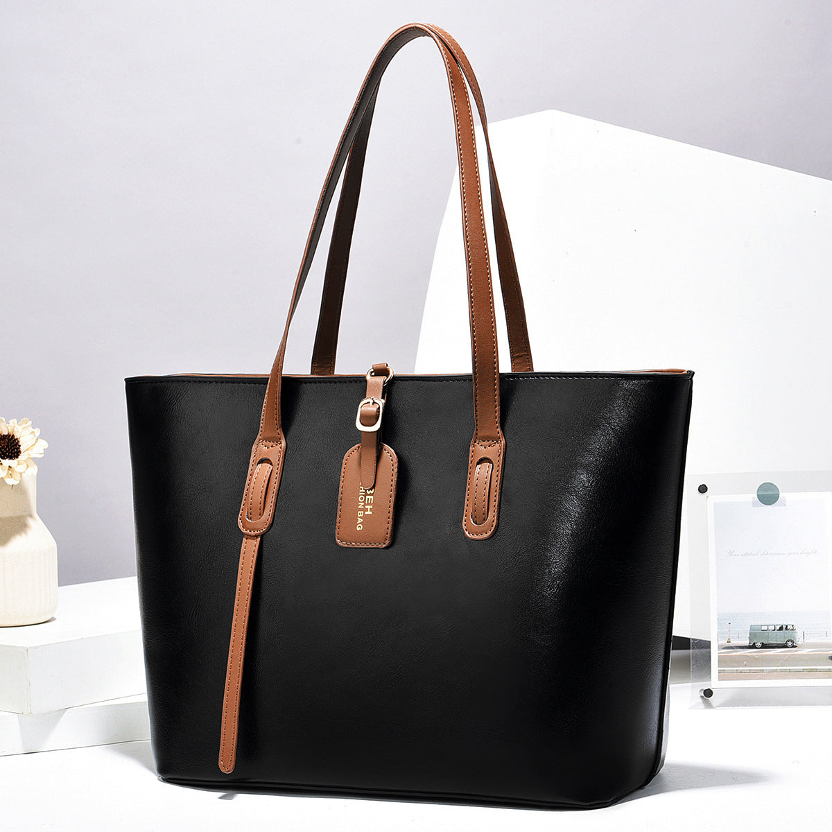 Black leather tote handbag with top handles and front zip pocket with zipper pull tab