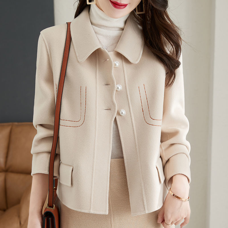 Woman wearing a beige coat with a brown handbag indoors