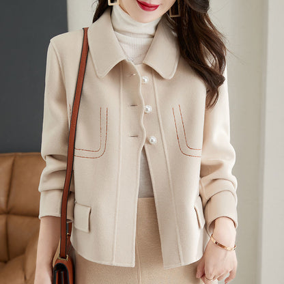 Woman wearing a beige coat with a brown handbag indoors