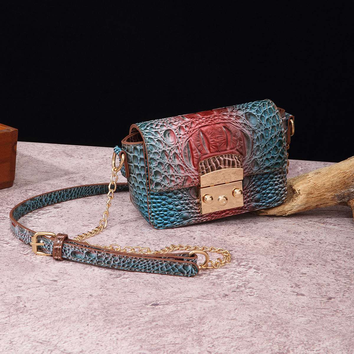 Blue crocodile-textured one-shoulder crossbody bag with red accent panel, gold-tone clasp, chain strap.
