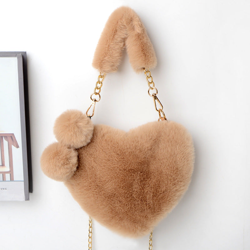 Tan plush heart shoulder bag with gold chain and fuzzy pom-pom accents.