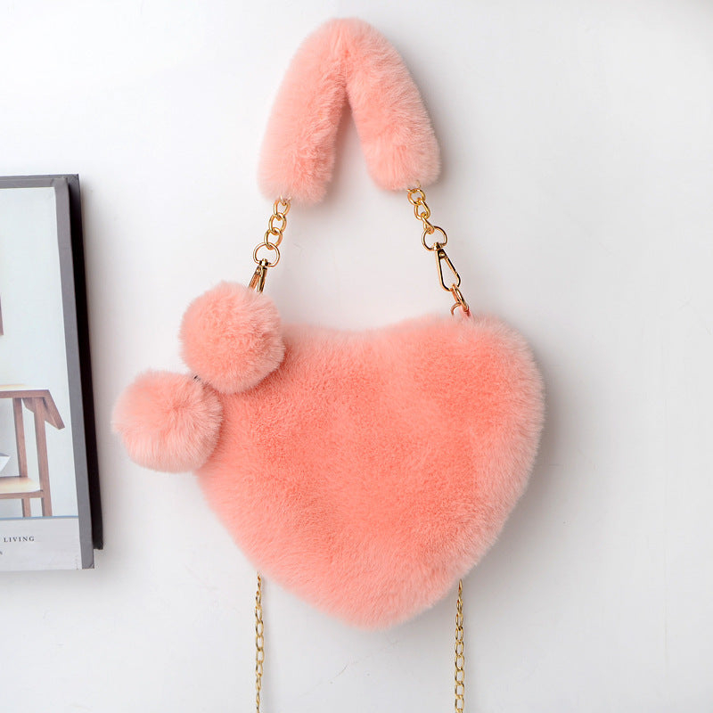 Heart-shaped plush handbag with pom-pom accents and gold chain strap, light pink