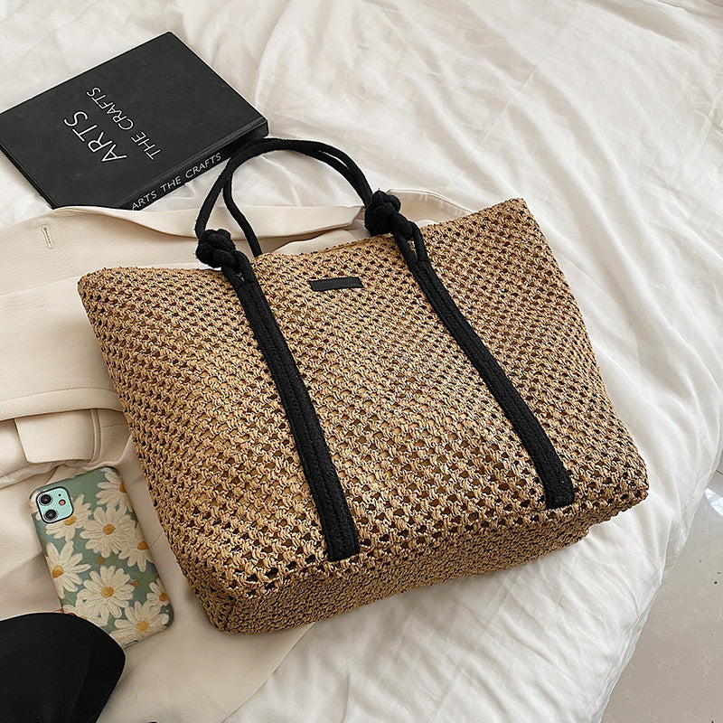 Tan woven tote bag with black rope handles and front logo plate