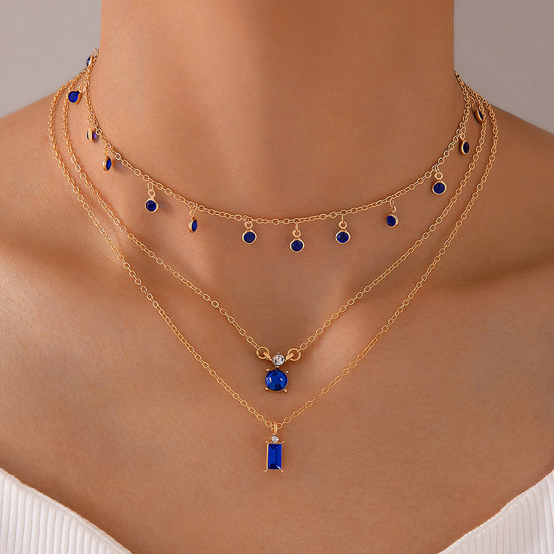 Multilayer necklace with gold chain, blue teardrop charms, and a blue bar pendant