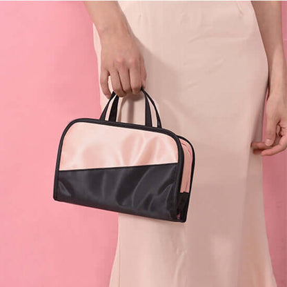 Cosmetic storage bag held by handle, black and pink body with zipper top.