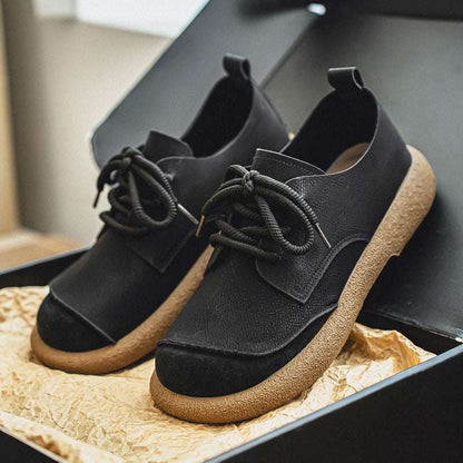 Black suede shoes with brown soles on a textured surface