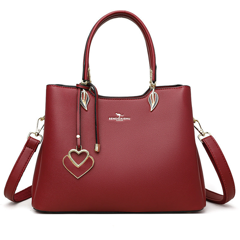Women's shoulder bag in wine red with top handles, heart charm, leaf pulls, and side straps