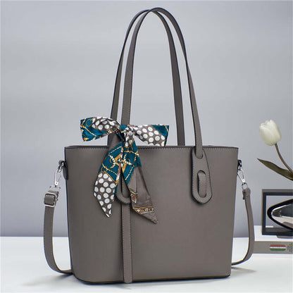 Gray tote handbag with top handles, front zipper pocket, and blue patterned bow at top.